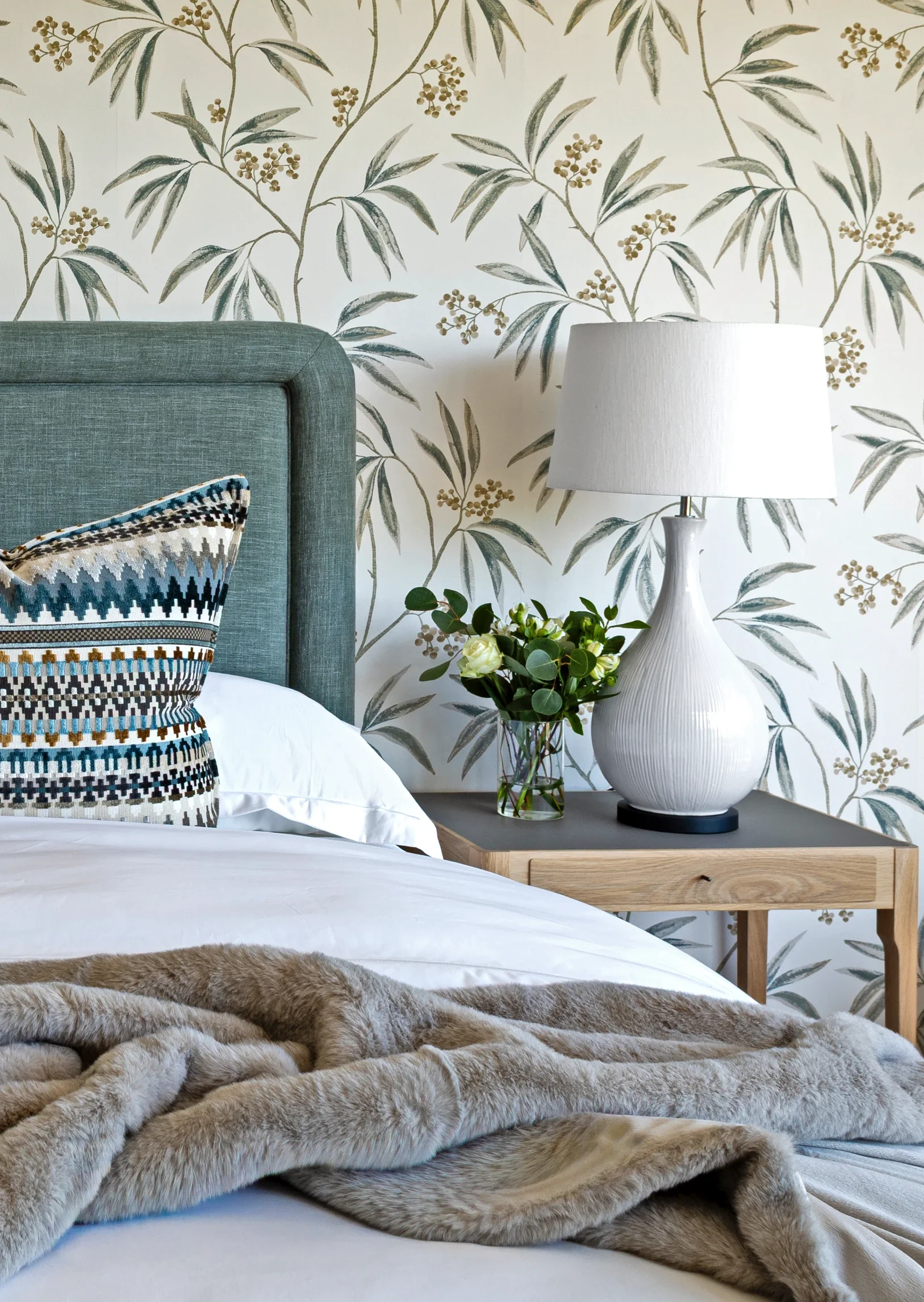 Main bedroom at The Glen: grey-blue headboard, botanical wallpaper, white ceramic lamp