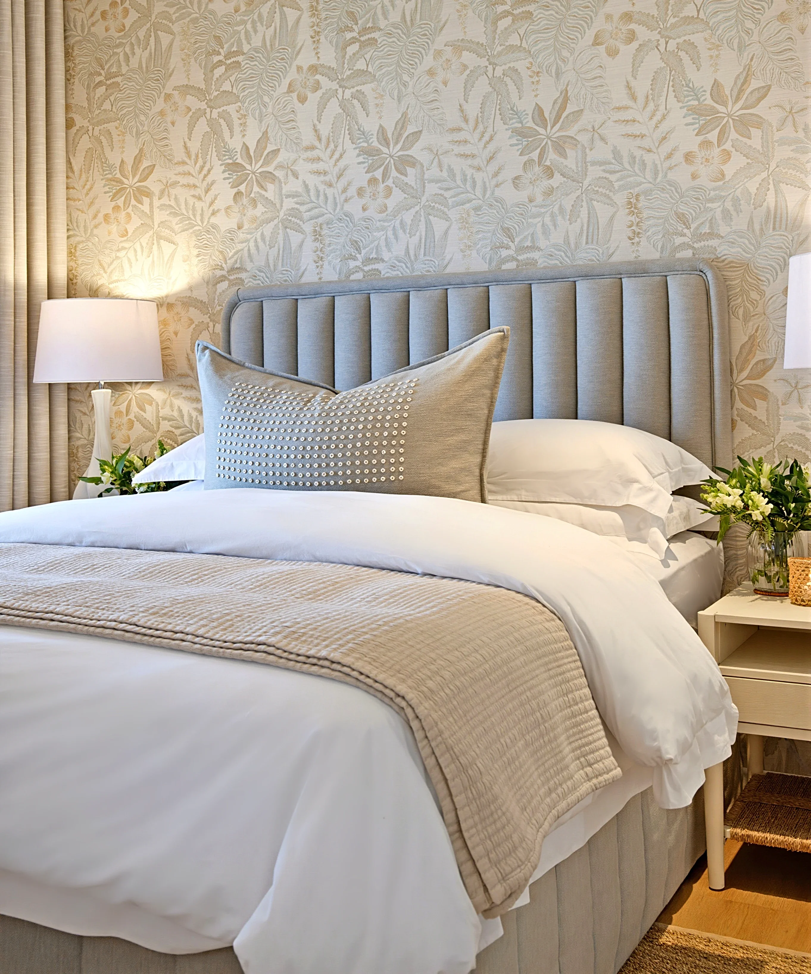 Main bedroom at Simbithi Eco-Estate: soft-toned tropical wallpaper, a fluted grey-blue headboard, white linen and tall ceramic lamps
