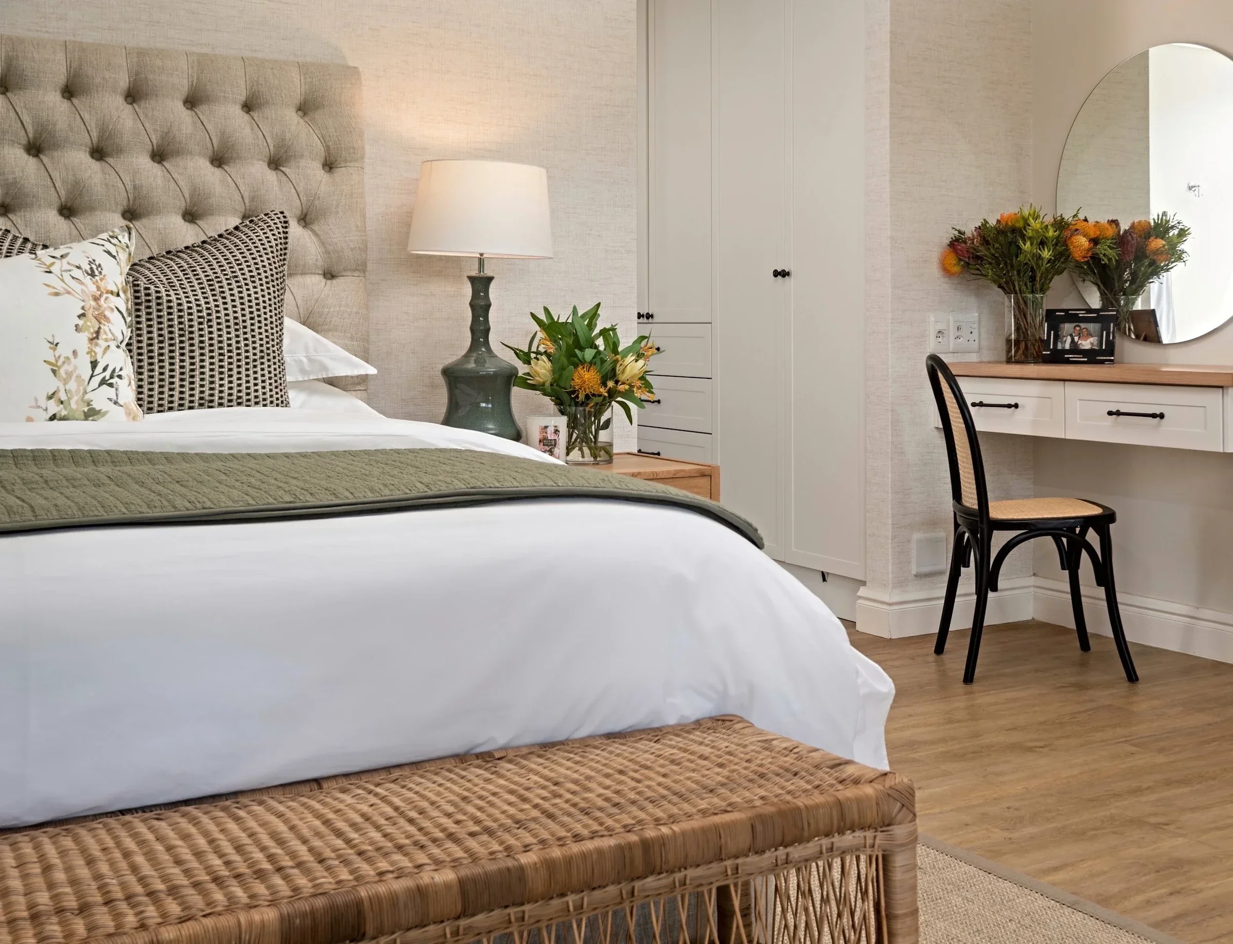 Main bedroom at Loxley Estate with a buttoned oatmeal headboard, a woven bench and a desk with a round mirror