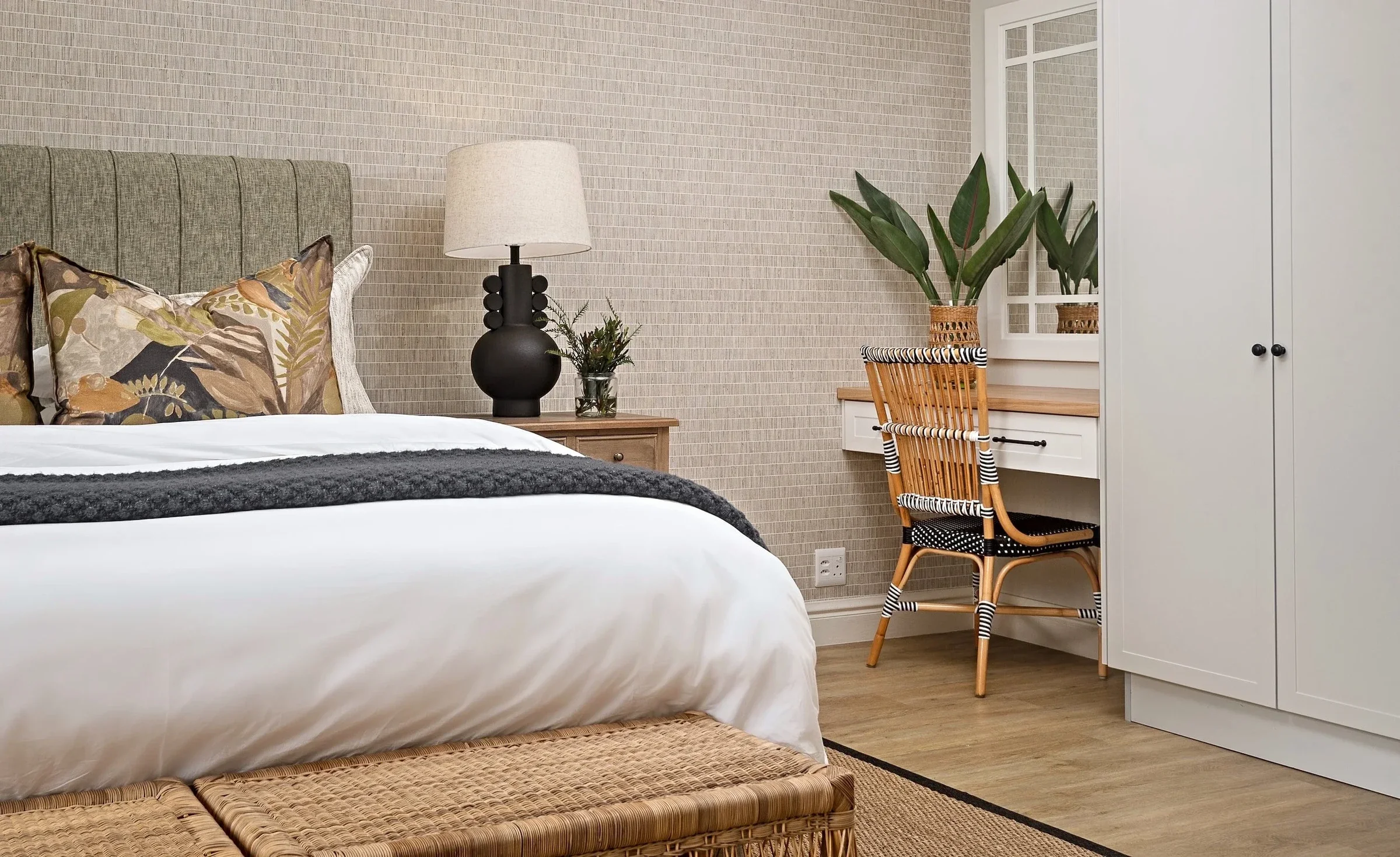 Guest bedroom at Loxley Estate with a green upholstered headboard, a woven bench and a rattan desk chair