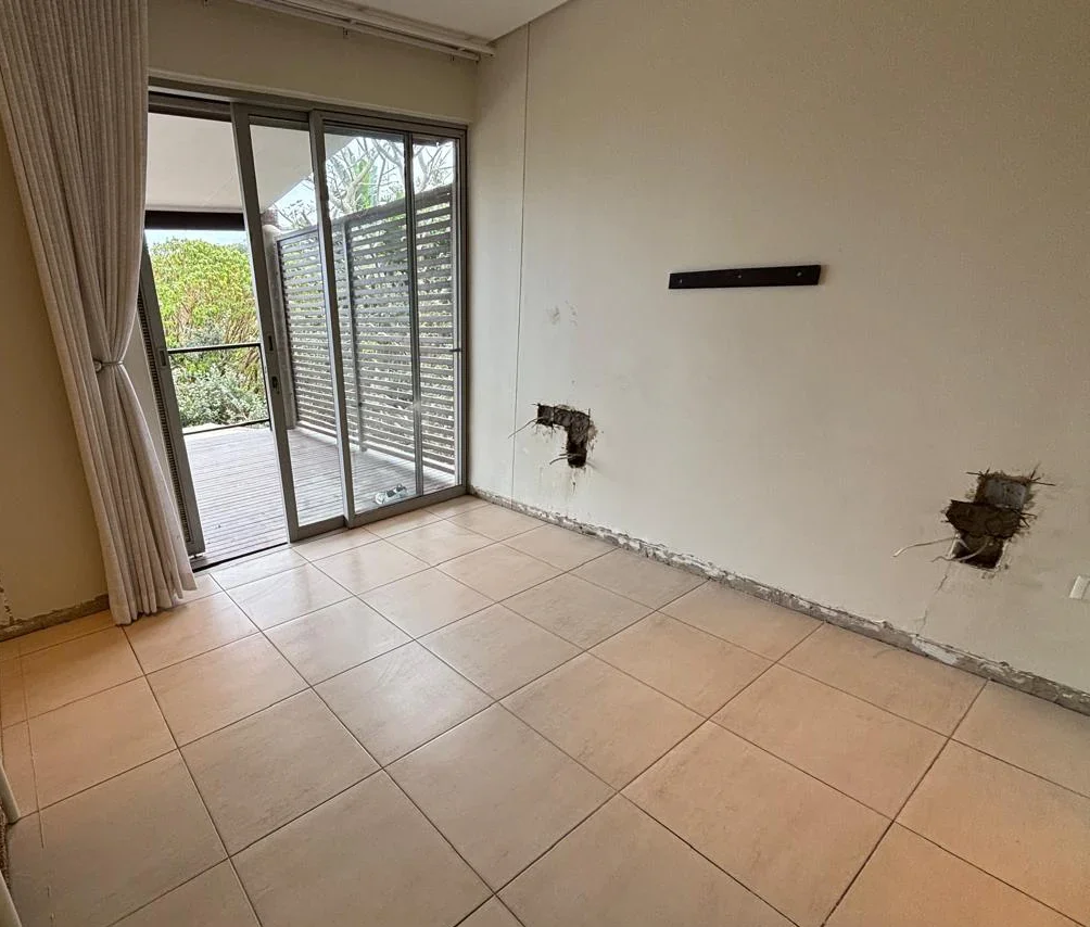 Main bedroom at Simbithi Eco-Estate before the renovation: beige floor tiles, cream walls and a sliding door to the deck