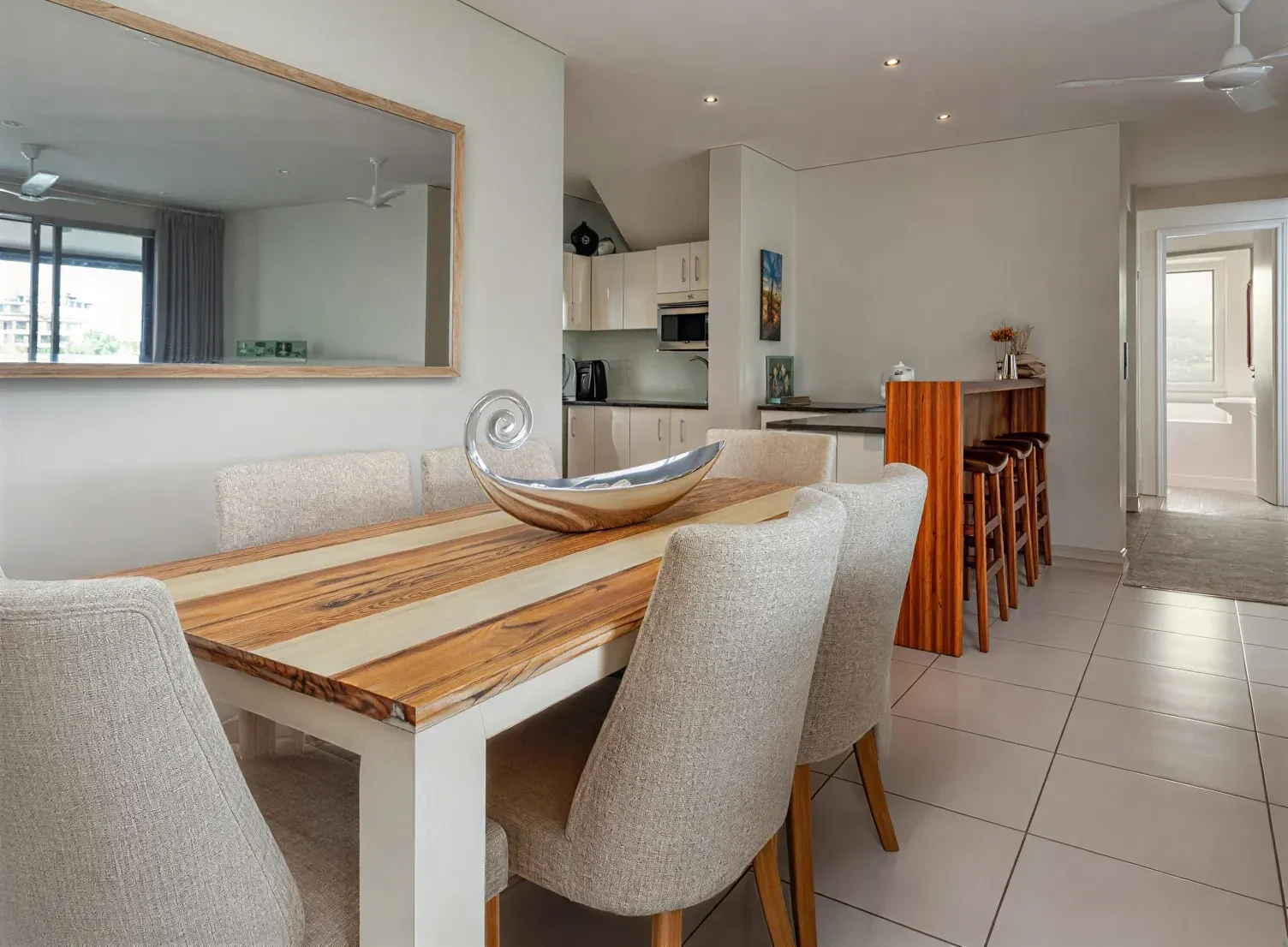Dining area at Simbithi Eco-Estate before the renovation: a striped timber table, oatmeal chairs, beige tiles and the old kitchen beyond