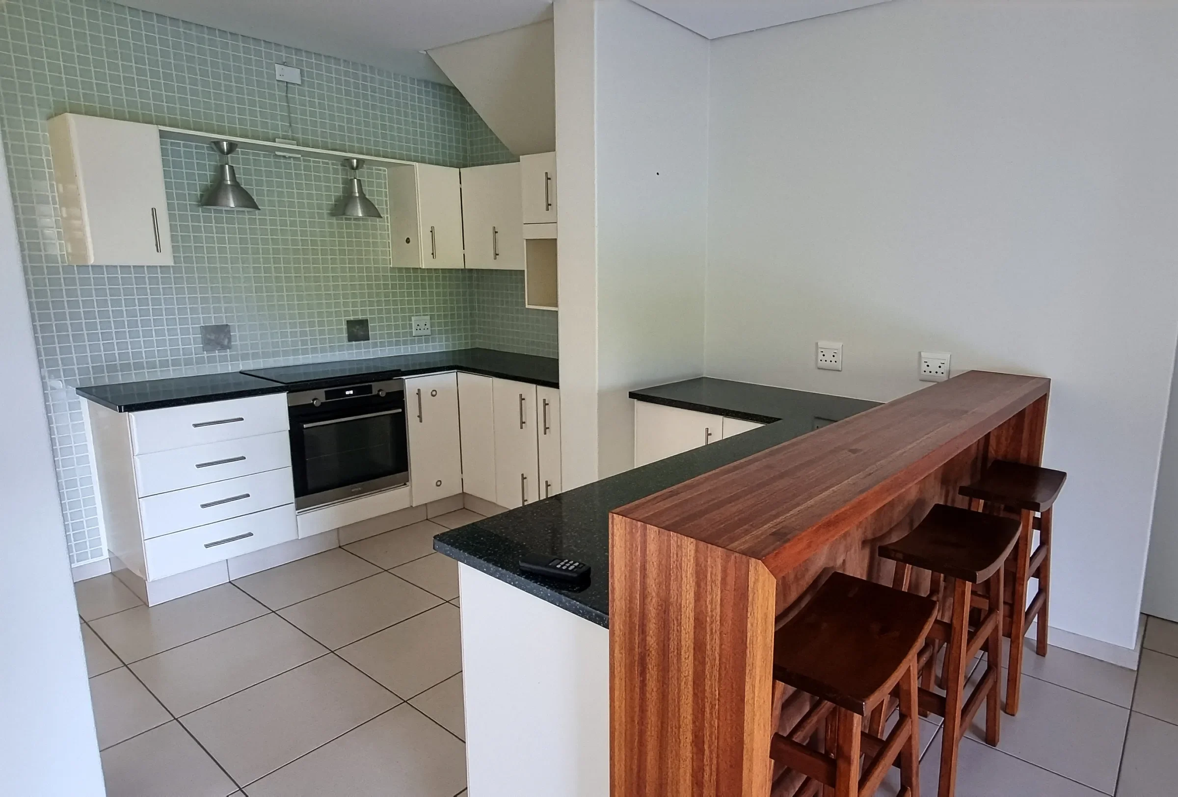 Kitchen at Simbithi Eco-Estate before the renovation: a green mosaic splashback, dark granite worktops, steel pendants and a timber breakfast bar