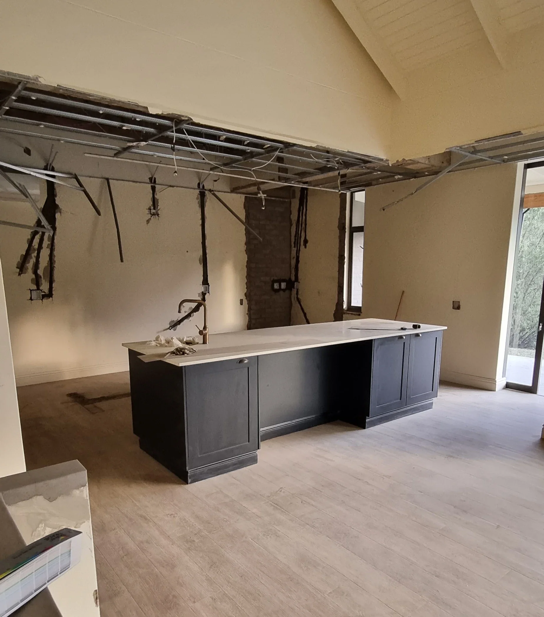 The kitchen at Loxley Estate, Sheffield Beach, before the work: the old kitchen stripped out, with the ceiling opened up and the dark island left in the empty room