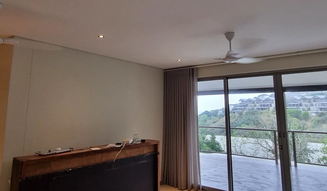 Living room at Simbithi Eco-Estate: a floating fluted television cabinet, curved cream armchairs, a glass coffee table and the terrace with sea views, before