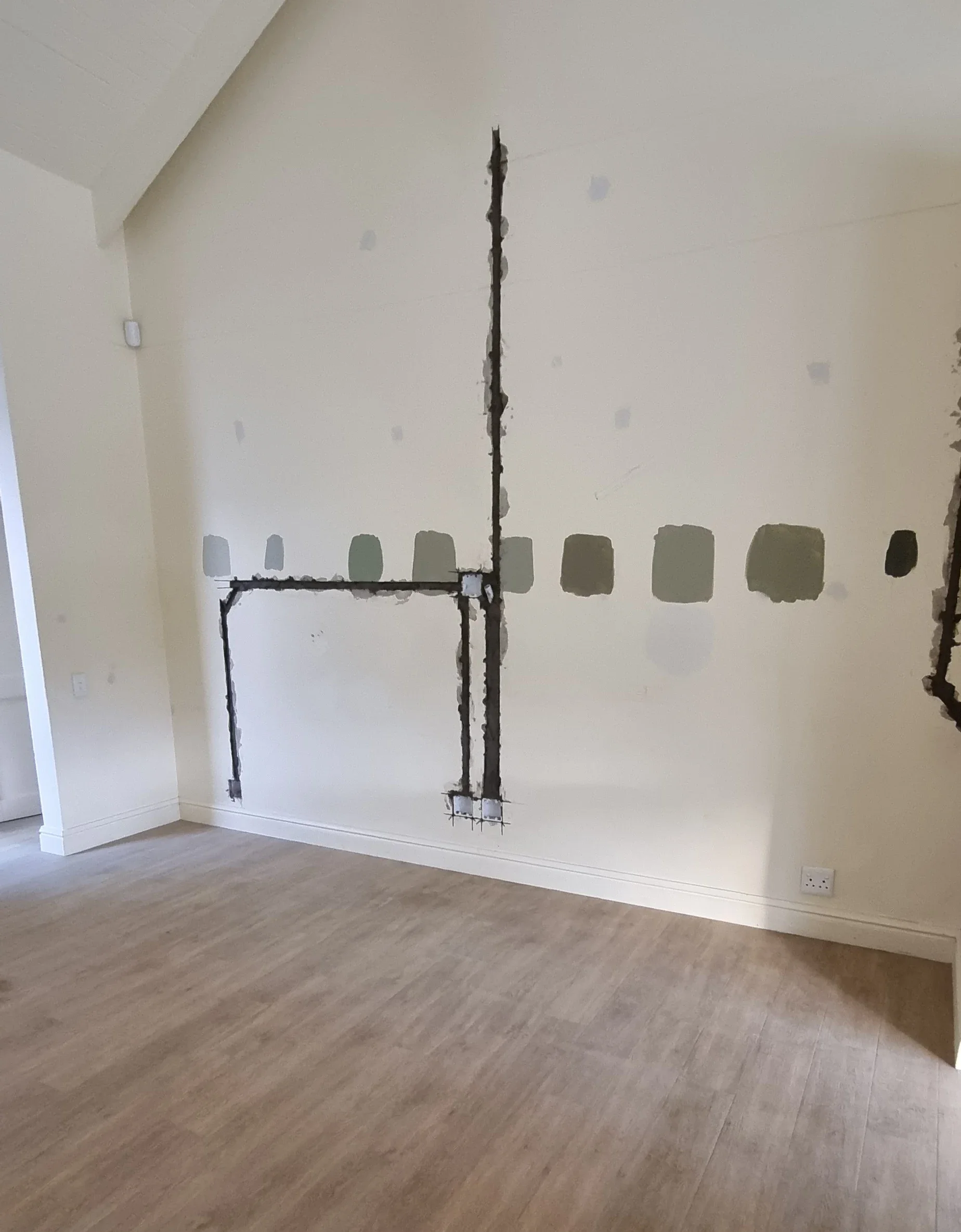 The living room at Loxley Estate before the work: an empty room with bare walls, exposed conduit and patched plaster where the television wall now stands