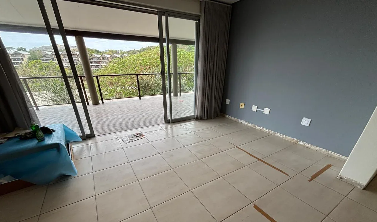 Living room at Simbithi Eco-Estate before the renovation: beige floor tiles, a slate-blue wall and grey curtains at the terrace doors