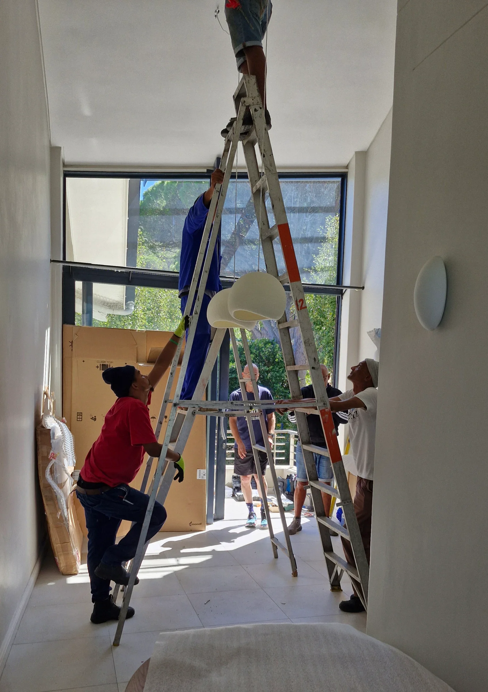The dining room at The Glen during the work: installers on tall ladders hanging the new pendant lights in front of the black-framed windows