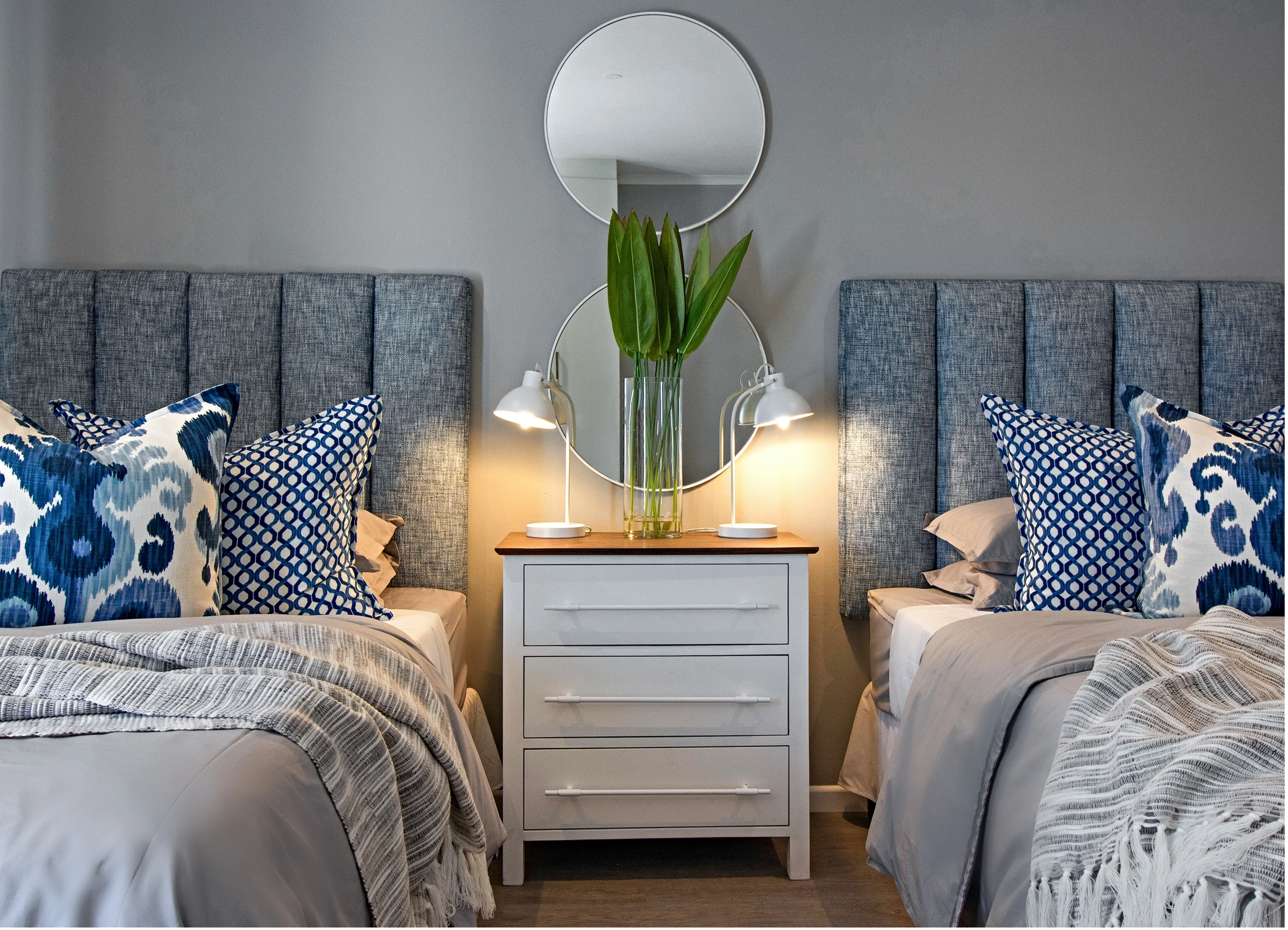 Girls' bedroom at Kenton-on-Sea: twin beds with grey upholstered headboards, blue and white patterned cushions and a white bedside chest