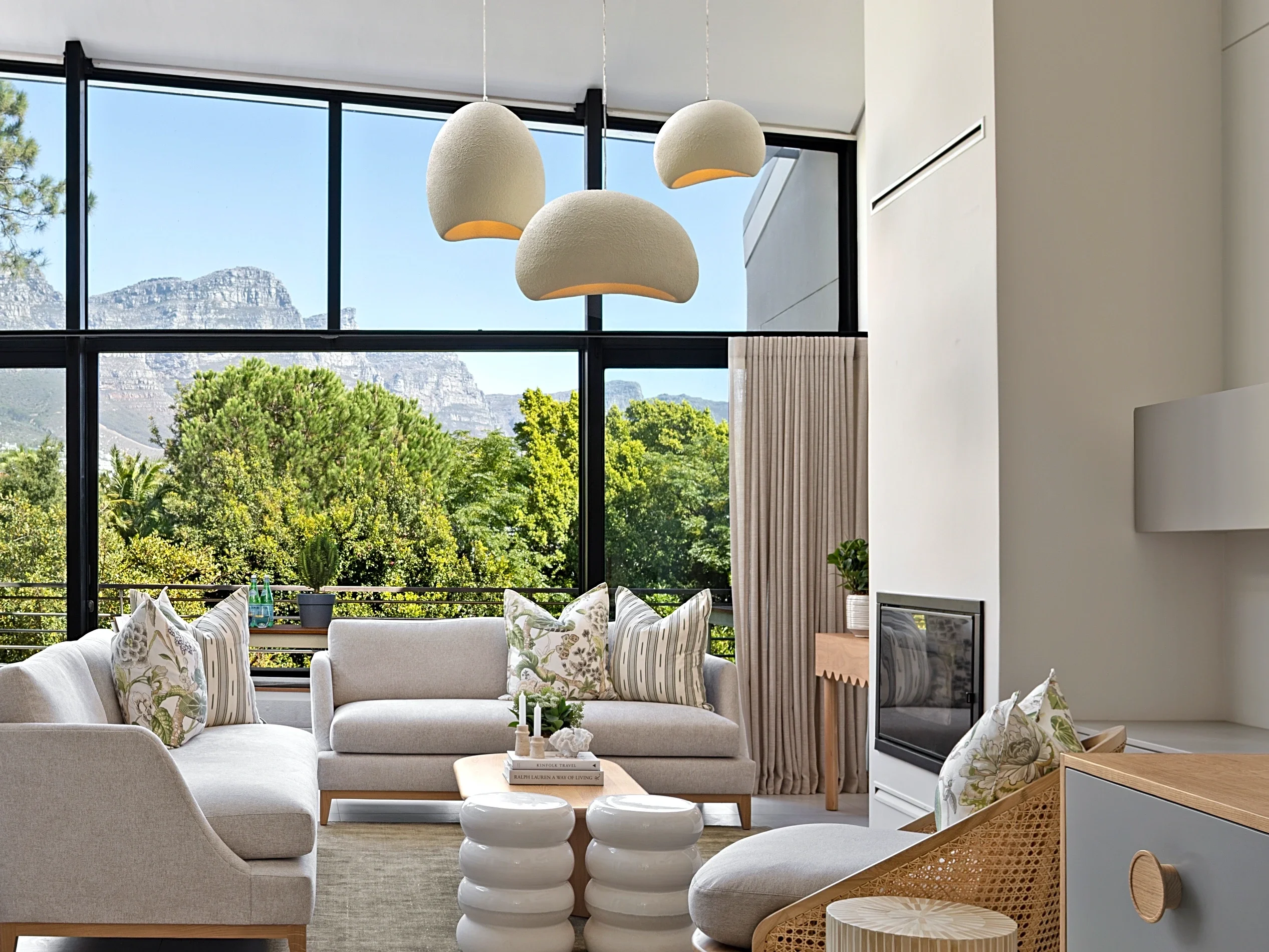 Living room at The Glen, Camps Bay: light sofas, three pendant lights and the mountain through the glass