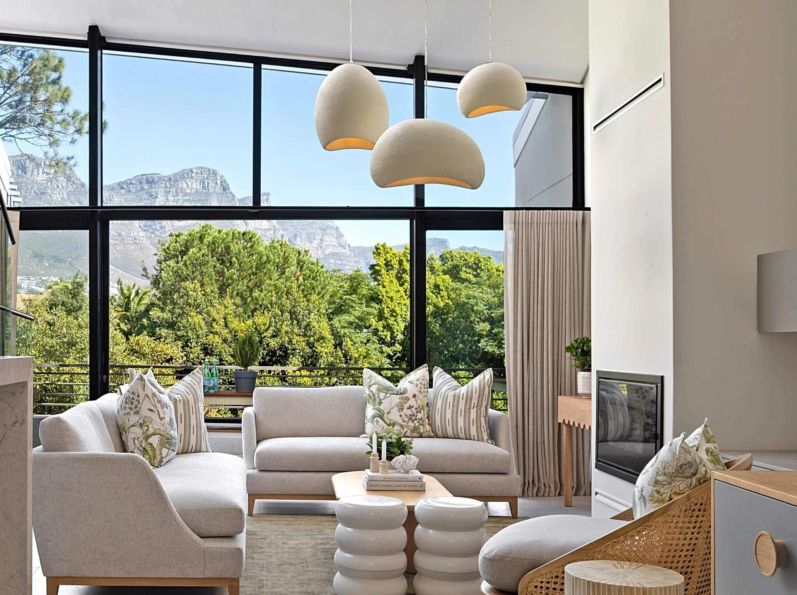 Living room at The Glen, Camps Bay: light sofas with botanical print cushions, three pendant lights and the mountain through the glass