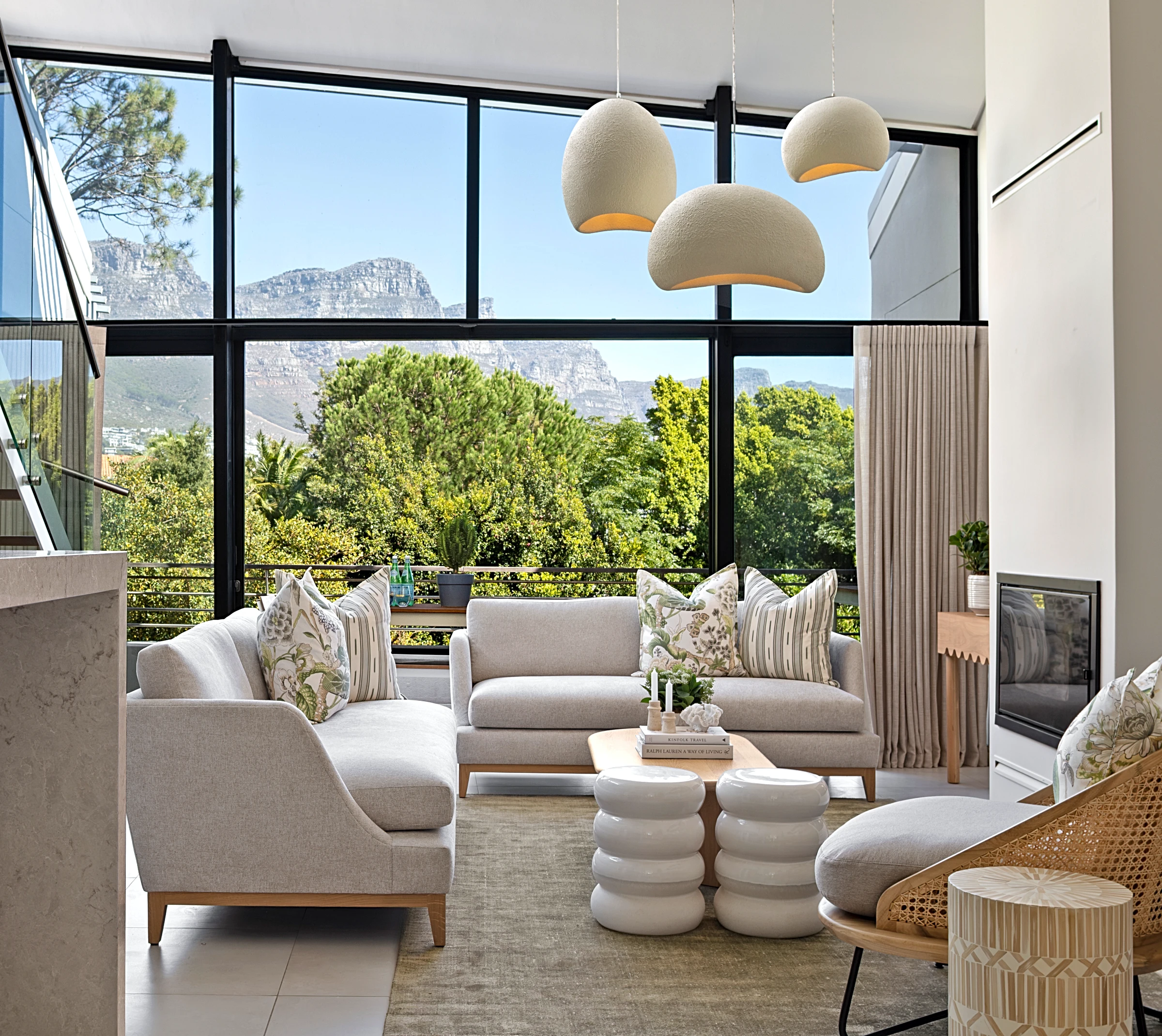 Living room at The Glen, Camps Bay: light sofas, three pendant lights and the mountain through the glass