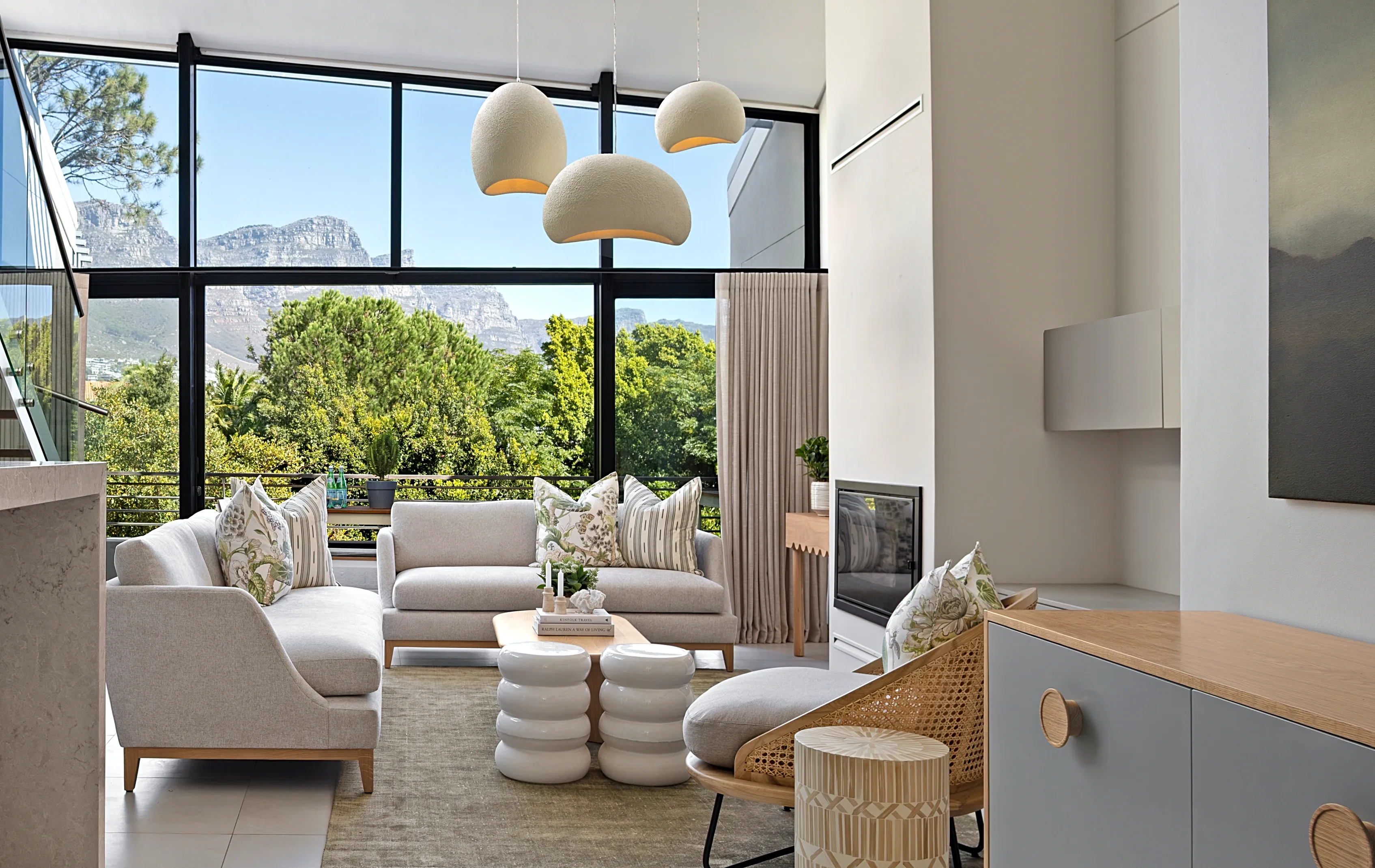 Living room at The Glen, Camps Bay: light sofas, three pendant lights and the mountain through the glass