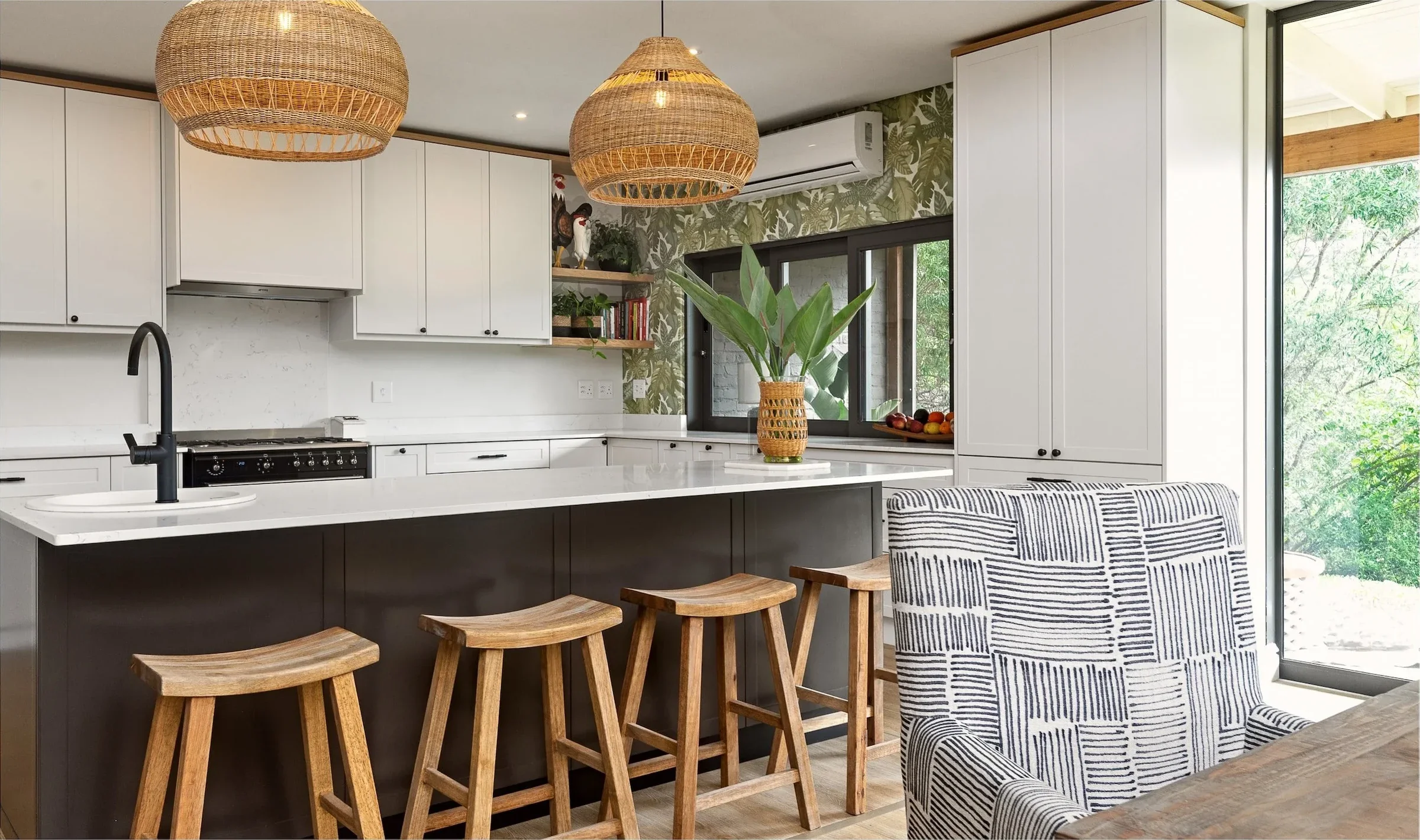 The finished kitchen at Loxley Estate: white cabinets, a charcoal island with timber stools and woven pendant lights