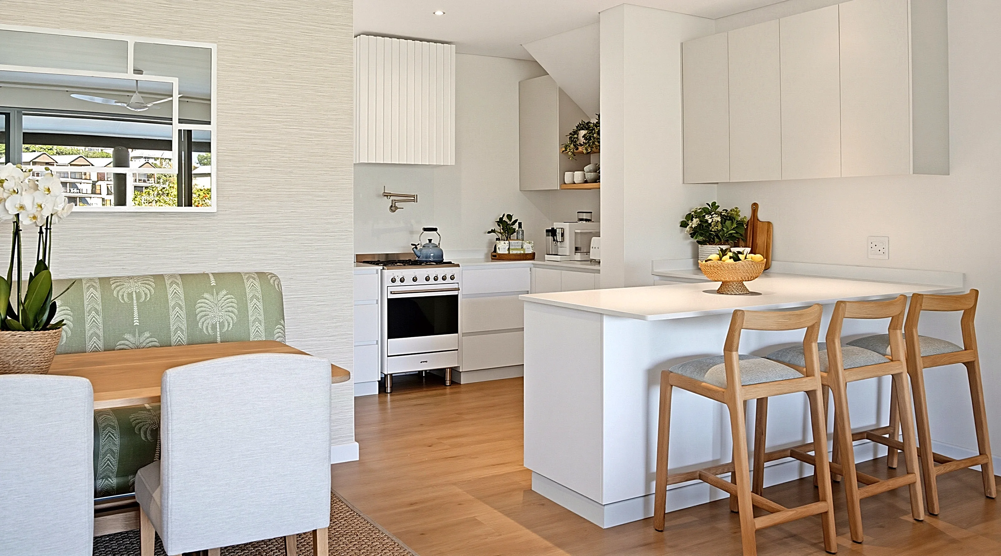 Kitchen at Simbithi Eco-Estate: a white quartz island with timber counter stools, soft grey wall cabinets, oak floating shelves and a stainless-steel range