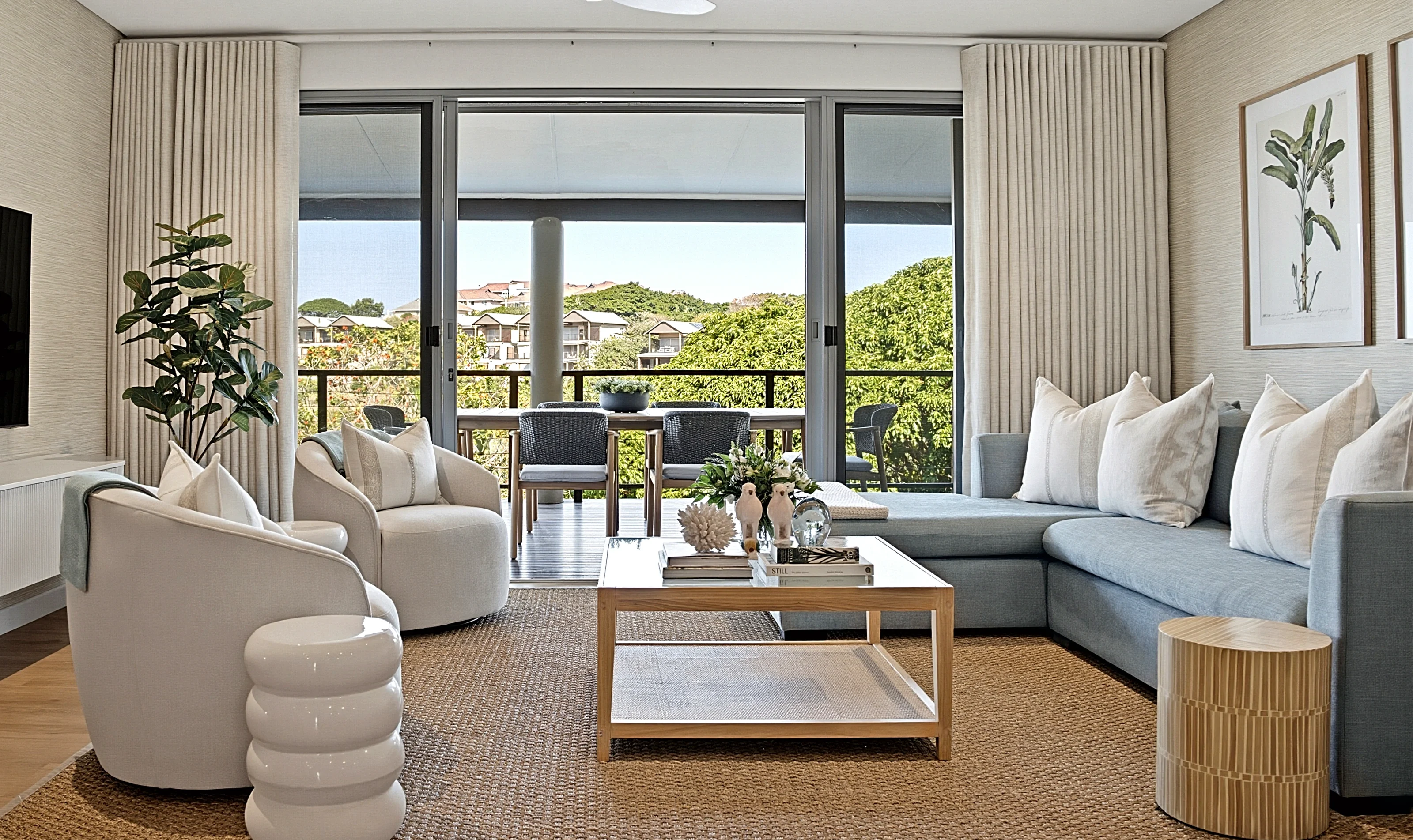 Living room at Simbithi Eco-Estate, Ballito: curved cream armchairs, a grey-blue sofa, a timber coffee table on a jute rug and the covered terrace beyond