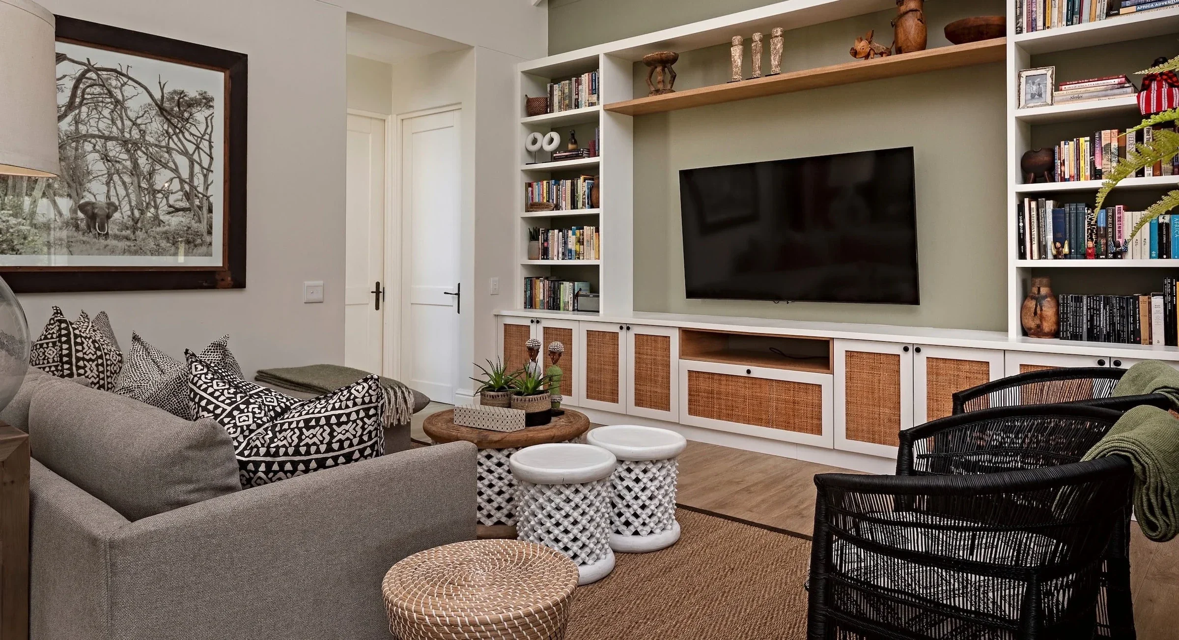 TV room at Loxley Estate, Sheffield Beach: built-in shelving around the television, a grey sofa with patterned cushions and a black cane armchair