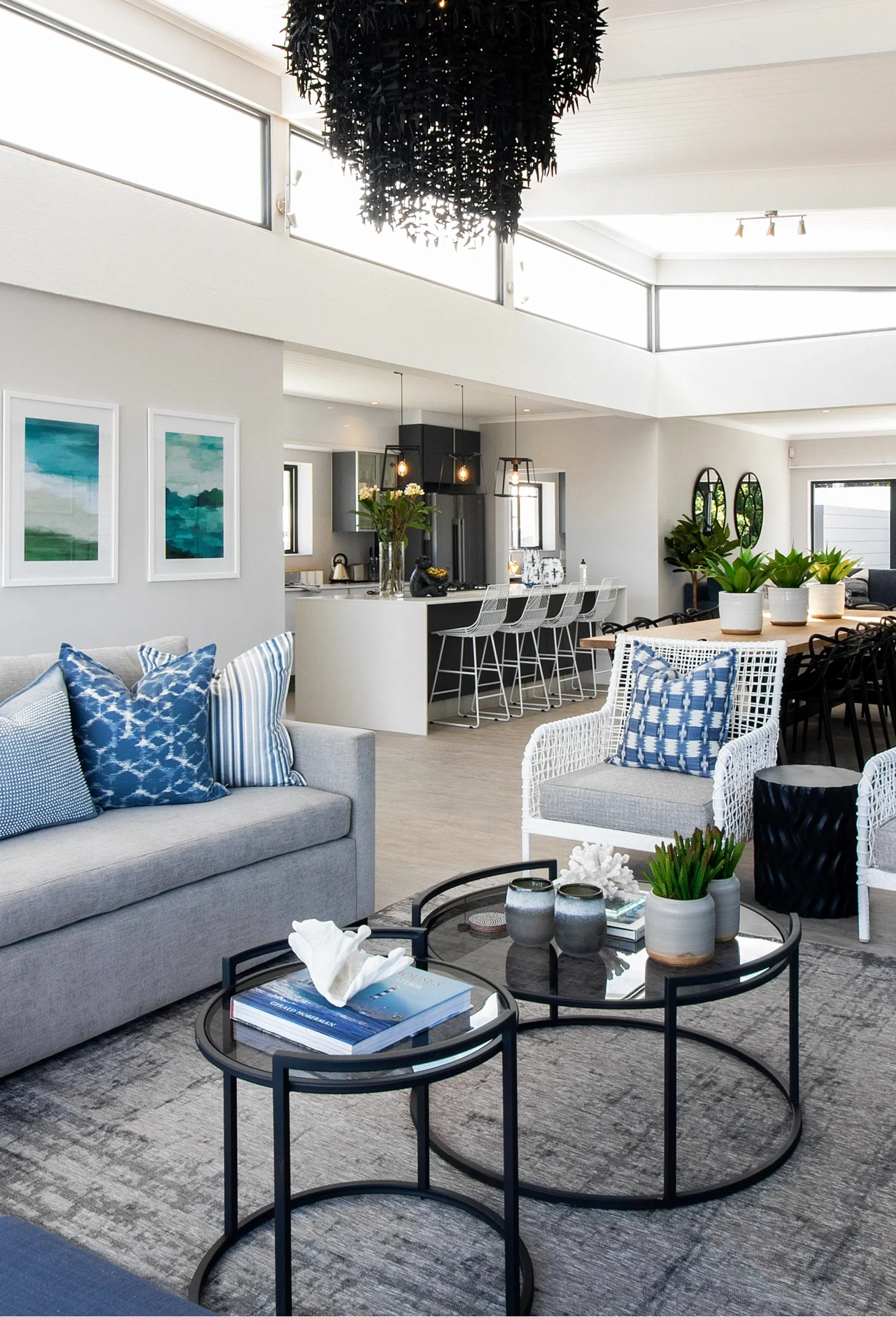 Open-plan living room and kitchen at Kenton-on-Sea: a grey sofa with blue patterned cushions, black nesting tables and a beaded chandelier