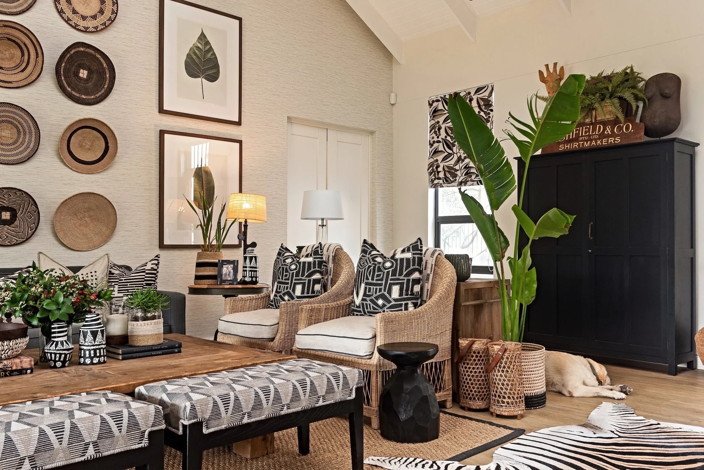 Living room at Loxley Estate, towards the forest: a wall of woven baskets, framed leaf prints and wicker armchairs with patterned cushions