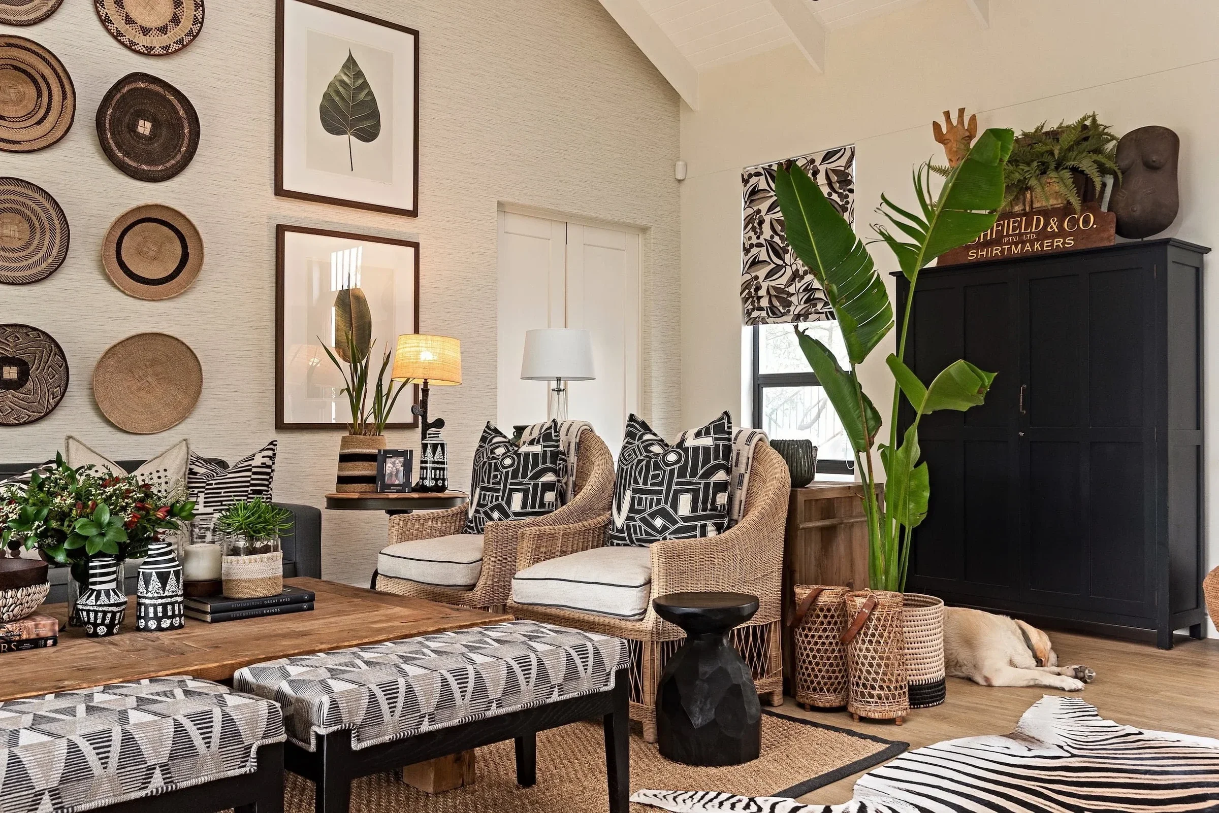 Living room at Loxley Estate, Sheffield Beach: a wall of woven baskets, framed leaf prints, wicker armchairs with black and white cushions and a black cabinet