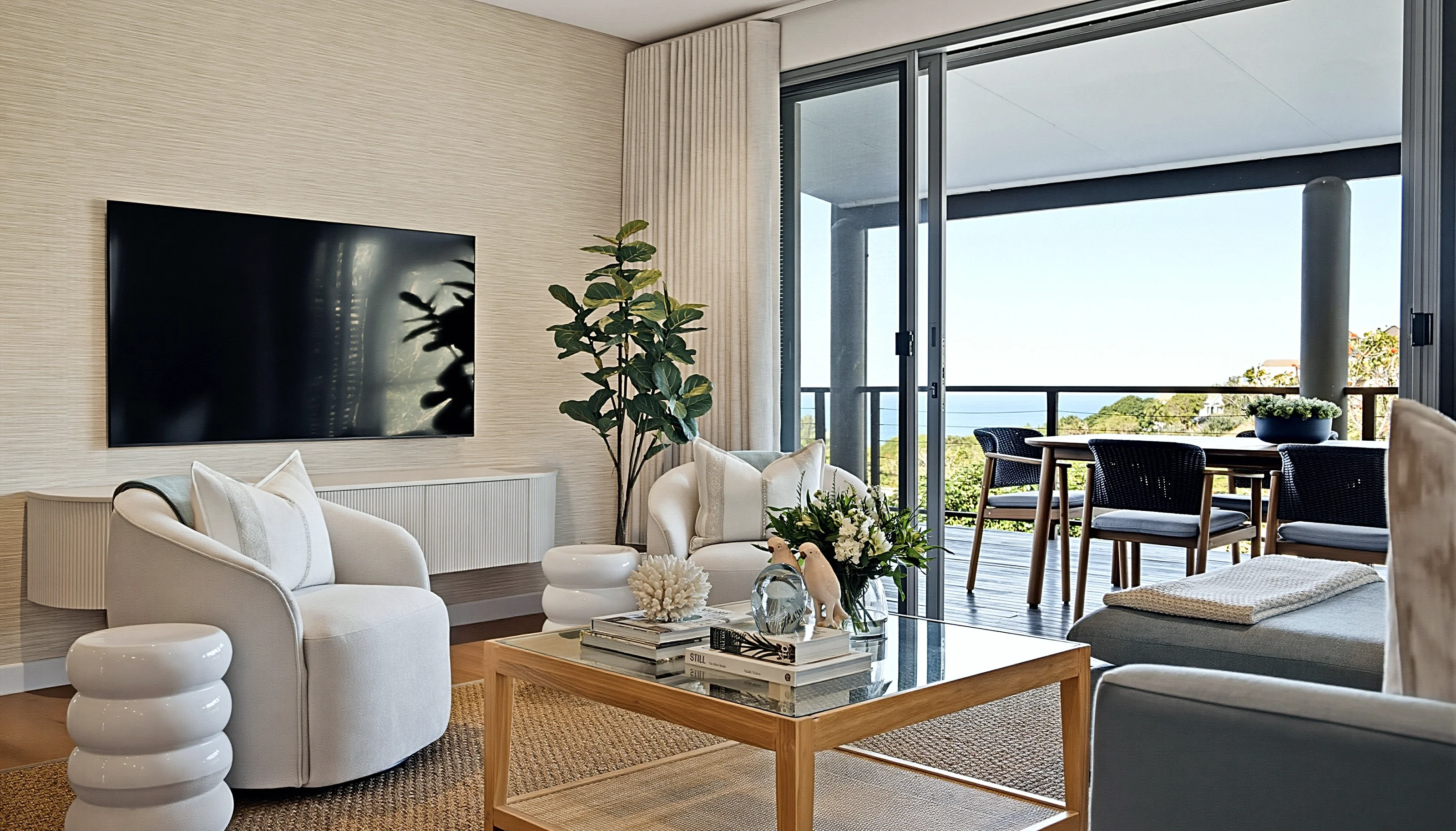 Living room at Simbithi Eco-Estate: a floating fluted television cabinet, curved cream armchairs, a glass coffee table and the terrace with sea views