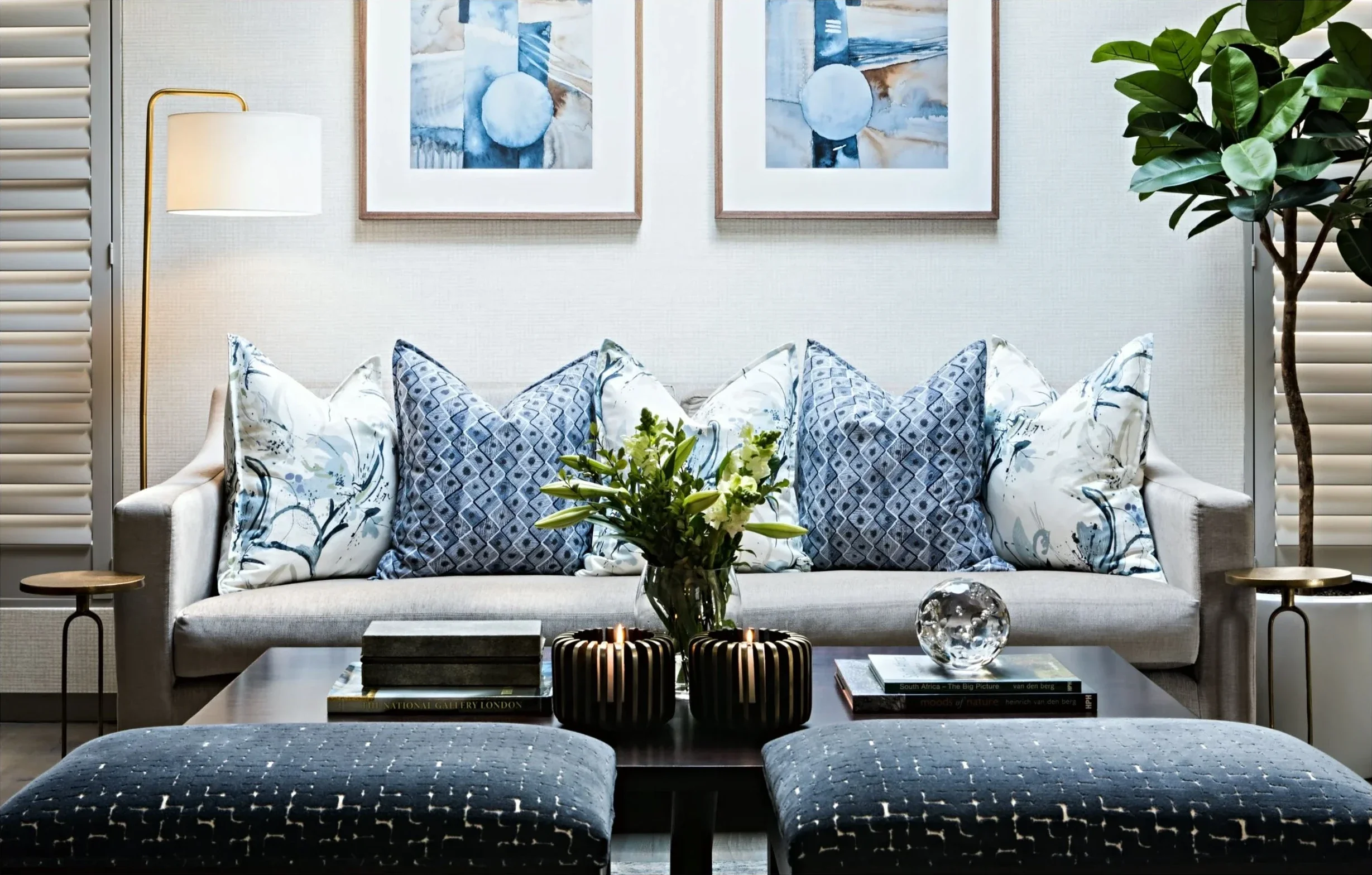 Living room with a light sofa, blue and white botanical cushions, a pair of framed blue prints and navy velvet ottomans