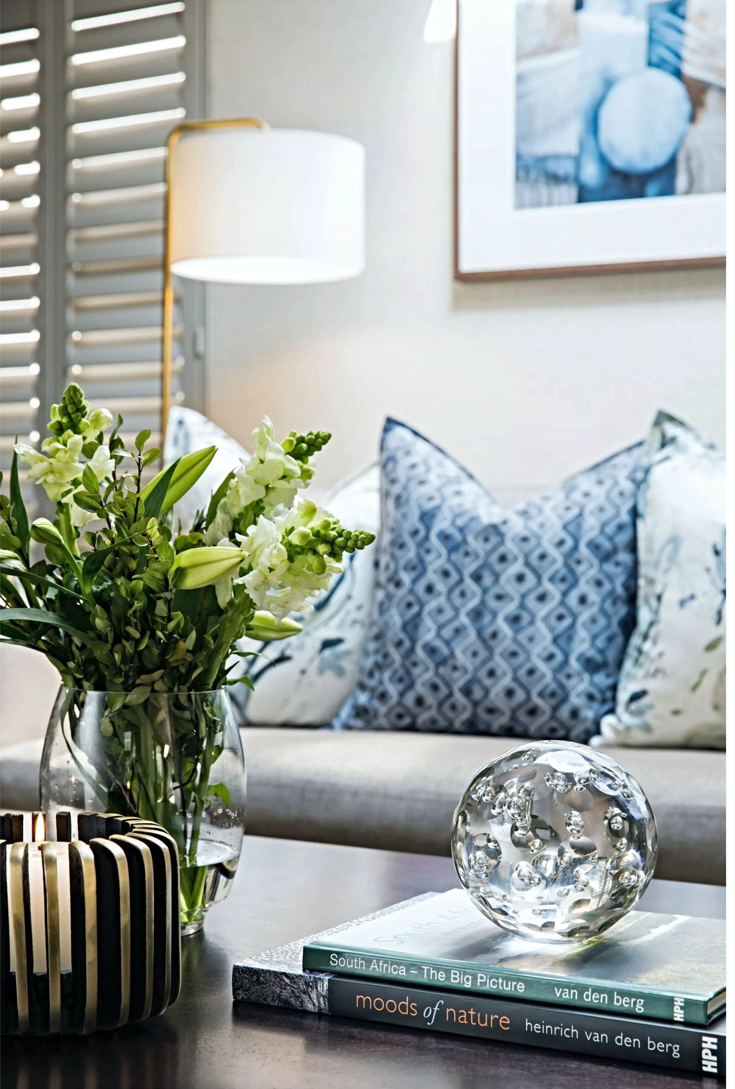 Detail of blue and white botanical cushions on a light sofa, with greenery and a framed blue print