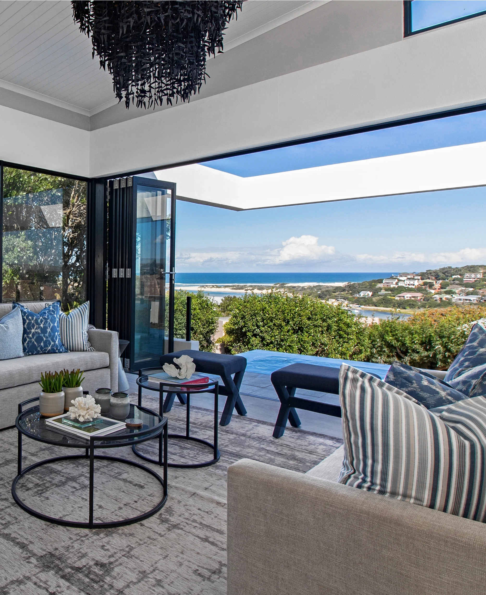 Living room at Kenton-on-Sea opening onto the covered terrace, with blue and white striped cushions and the sea beyond