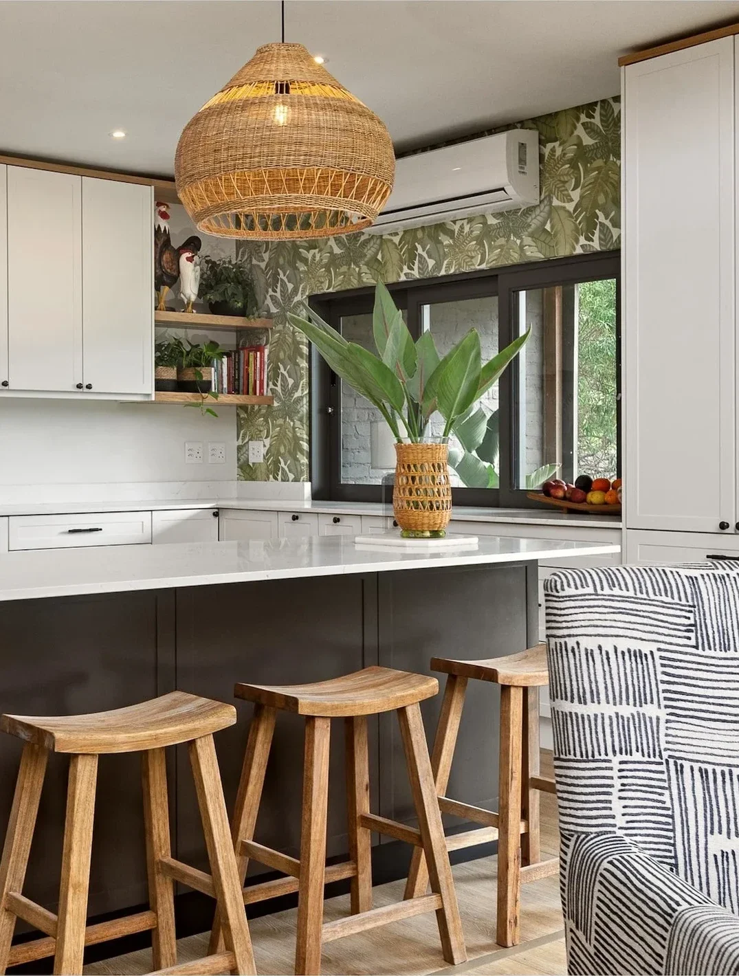 Kitchen at Loxley Estate: a woven pendant above a charcoal island with timber stools, white cabinets and leafy wallpaper around the window
