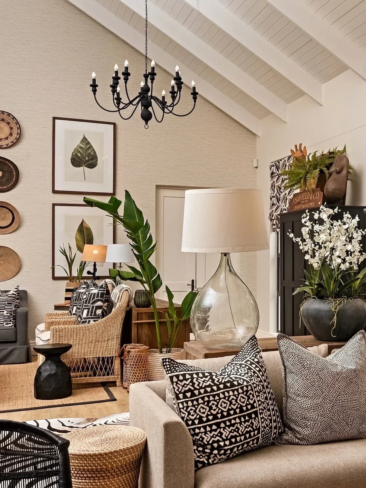 Living room at Loxley Estate: a black chandelier, framed leaf prints, a glass lamp, a black cabinet with white orchids and patterned black and white cushions