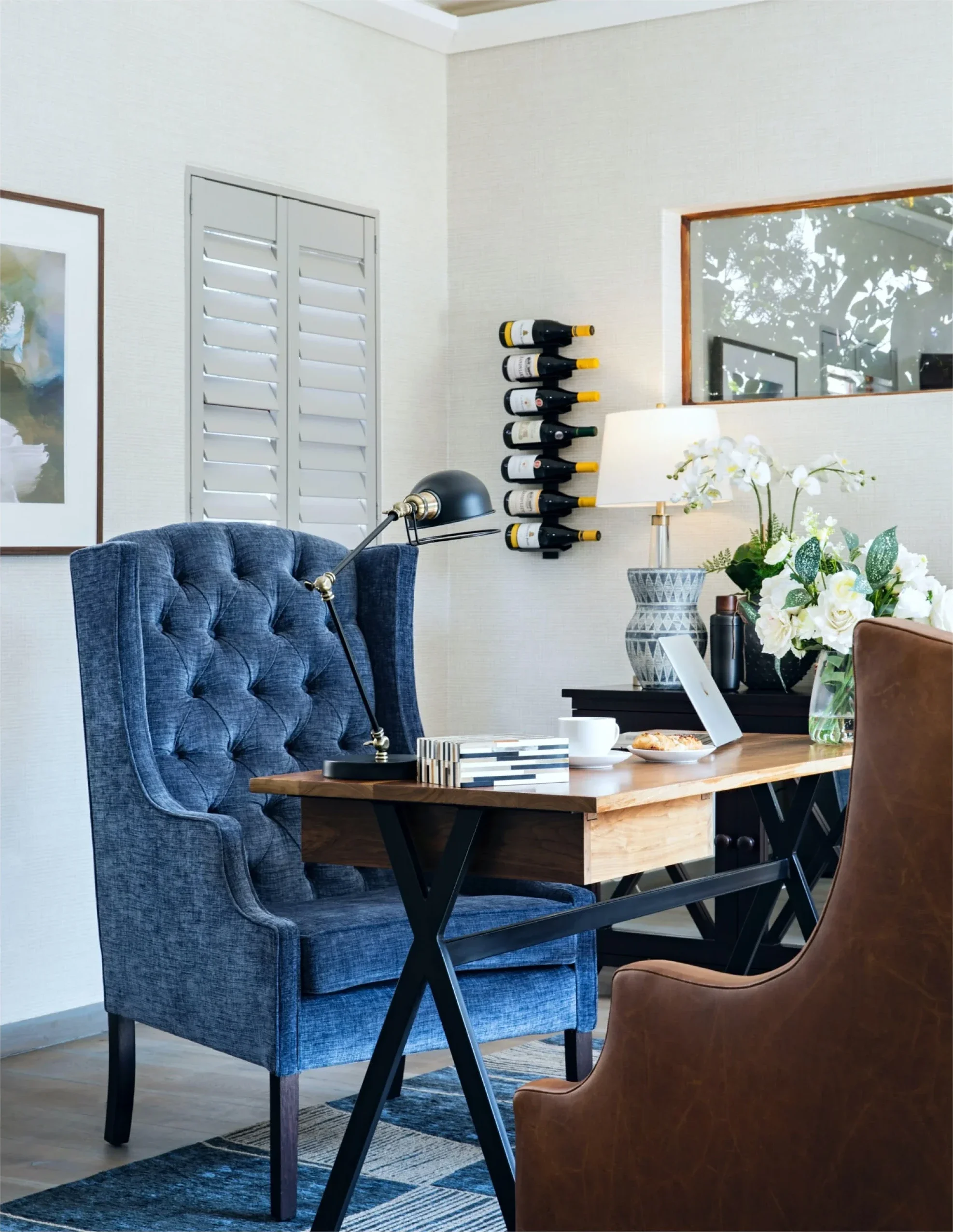 Study corner with a navy buttoned chair at a timber desk, flowers and framed prints
